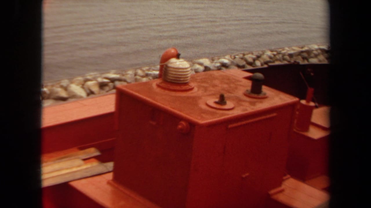 1971 Long Beach 8mm frame showing a red railroad maintenance vehicle deck, large housing, coiled hose, and gravel-lined edge beyond.