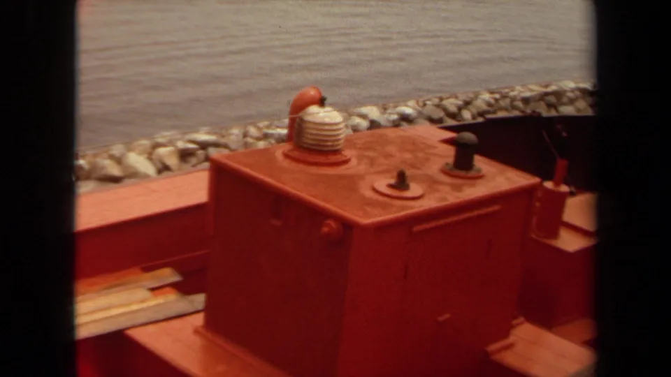 1971 Long Beach 8mm frame showing a red railroad maintenance vehicle deck, large housing, coiled hose, and gravel-lined edge beyond.