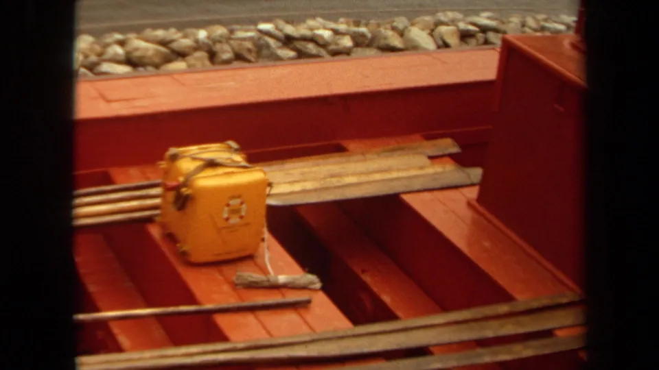 Close 8mm view of a yellow toolbox, long metal rods, and planks on a red maintenance vehicle deck in 1971 Long Beach.