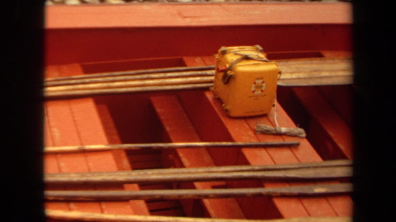 1971 Long Beach 8mm frame showing a red-painted boat interior with fishing rods, a yellow tackle box, and loose gear on deck.