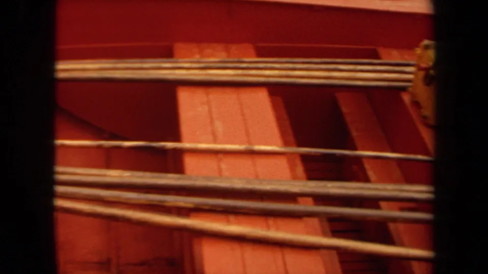 1971 Long Beach 8mm frame of rods or poles laid across a red wooden boat interior, with a yellow tackle box partly visible.