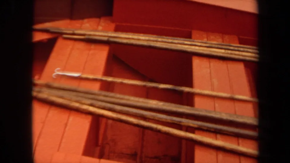 1971 Long Beach 8mm frame showing a red boat deck with grouped rods or poles and a metal hook lying nearby.