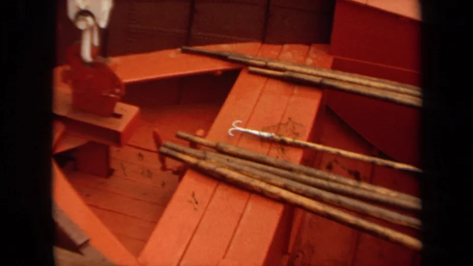 1971 Long Beach 8mm frame of a red-painted fishing boat interior with rods, a hook, and built-in wooden fittings visible.