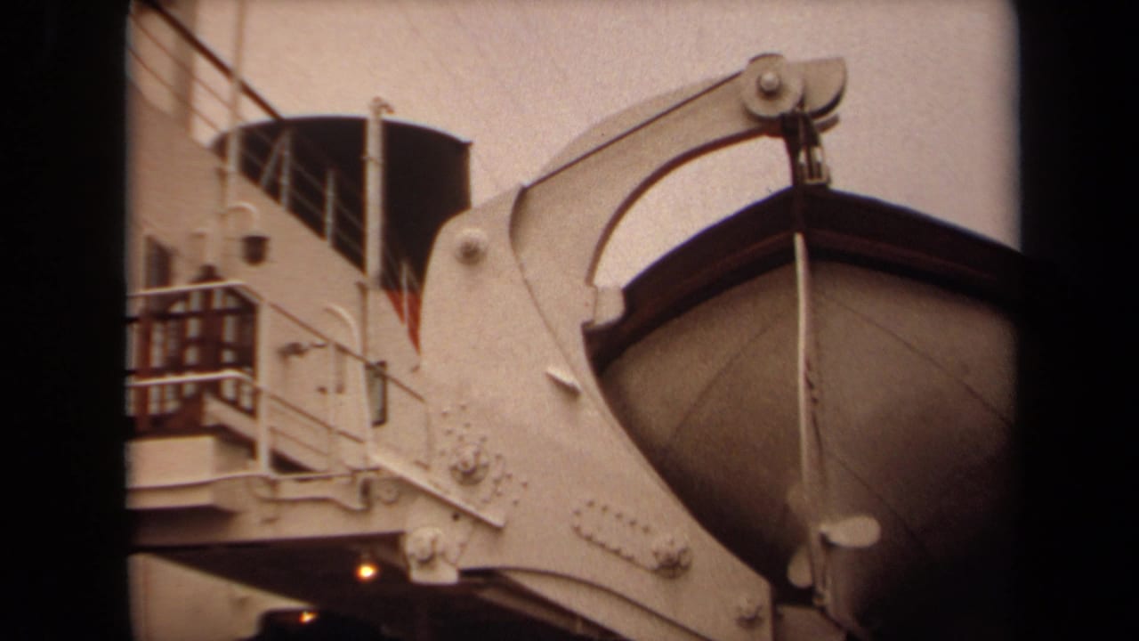 1971 Long Beach 8mm frame showing a lifeboat hanging from a shipboard davit against a white vessel structure.