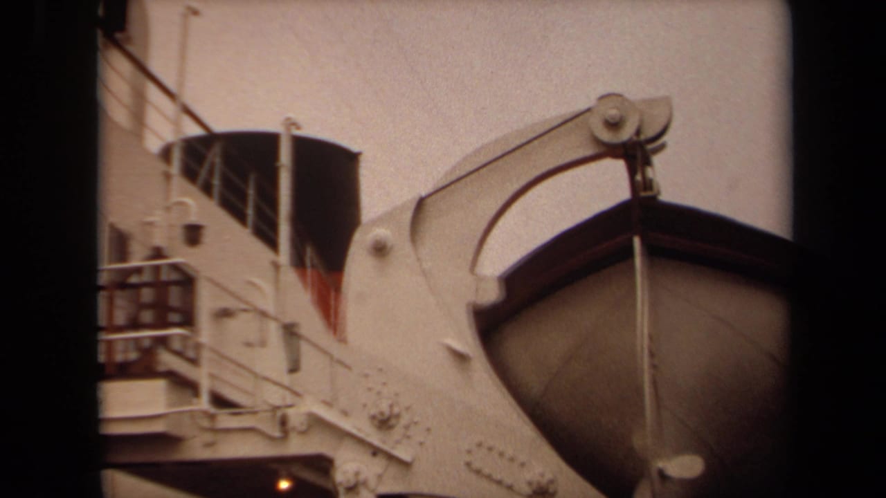 Close view of a lifeboat being lowered from a ship davit near railings and a dark vent.