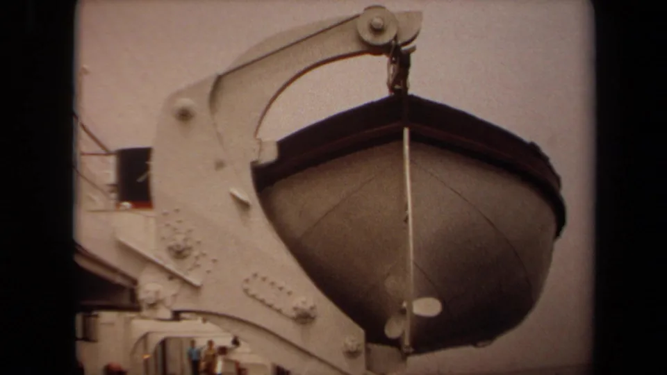 1971 Long Beach 8mm frame showing the lifeboat beside the davit, with small deck figures visible below.