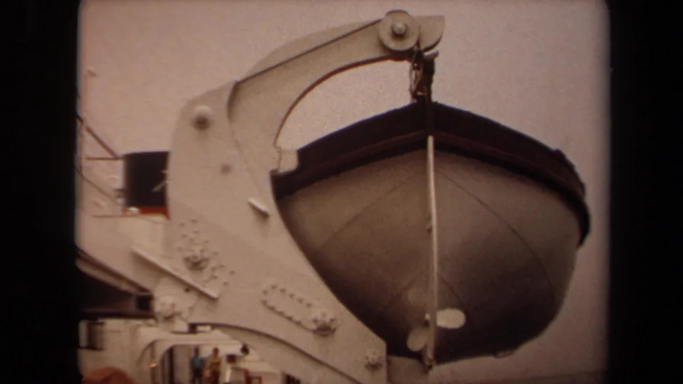 1971 Long Beach home-movie frame showing a lifeboat suspended from a white ship davit with passengers or visitors partly visible below.