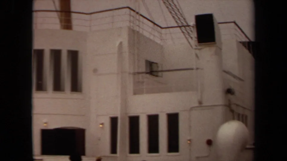 1971 Long Beach frame with the white curved exterior, tall dark windows, railings, and small visitor figures along the lower edge.