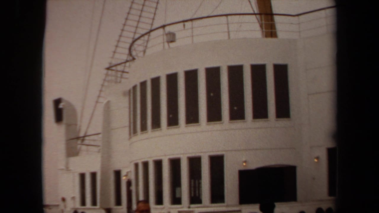 White ship exterior with curved windows and railings seen from a deck-level angle.