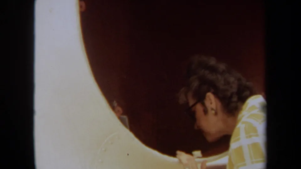 Close 1971 Long Beach home-movie view of the woman in profile as she peers near the red circular ship opening.