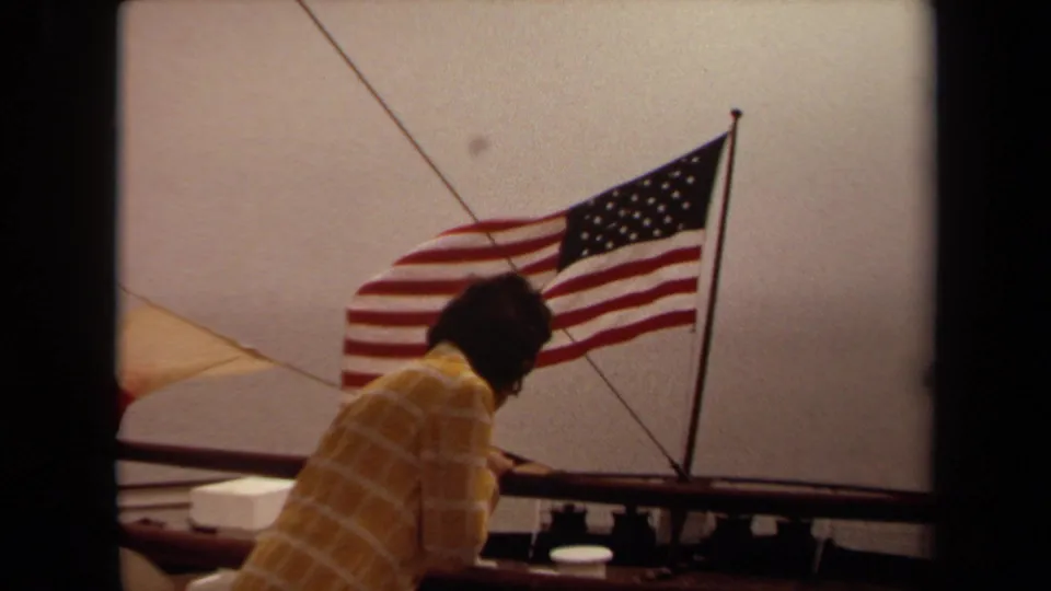 1971 Long Beach boating frame with a person seen from behind and an American flag moving in the wind.