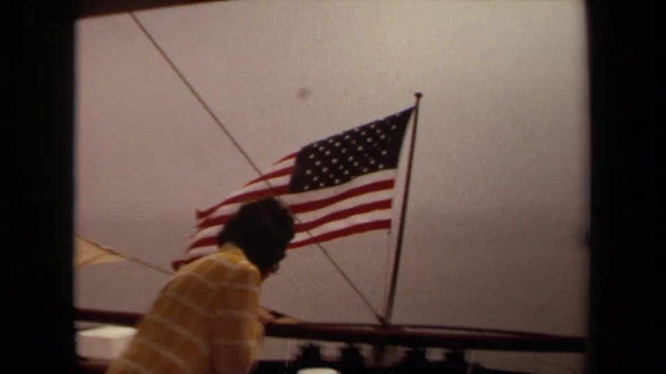 1971 Long Beach 8mm frame showing a boat-deck view with a person, rail, rigging and American flag.