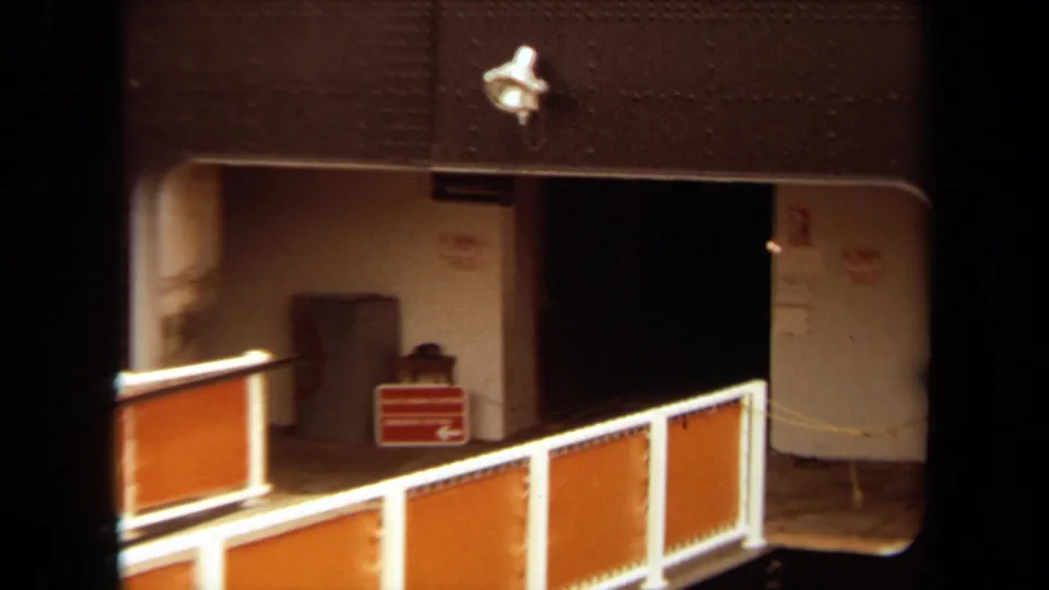 1971 Long Beach dockside view with an orange-railed gangway crossing in front of a large ship entry and red directional signage.