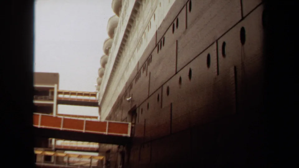 1971 Long Beach frame of a large vessel or maritime structure, showing the hull, portholes, upper deck, and connector walkway from below.