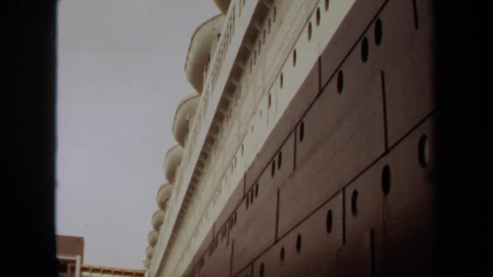 1971 Long Beach frame showing the side of a large vessel or maritime structure, with portholes, pale upper deck, and dockside elements at the edge.