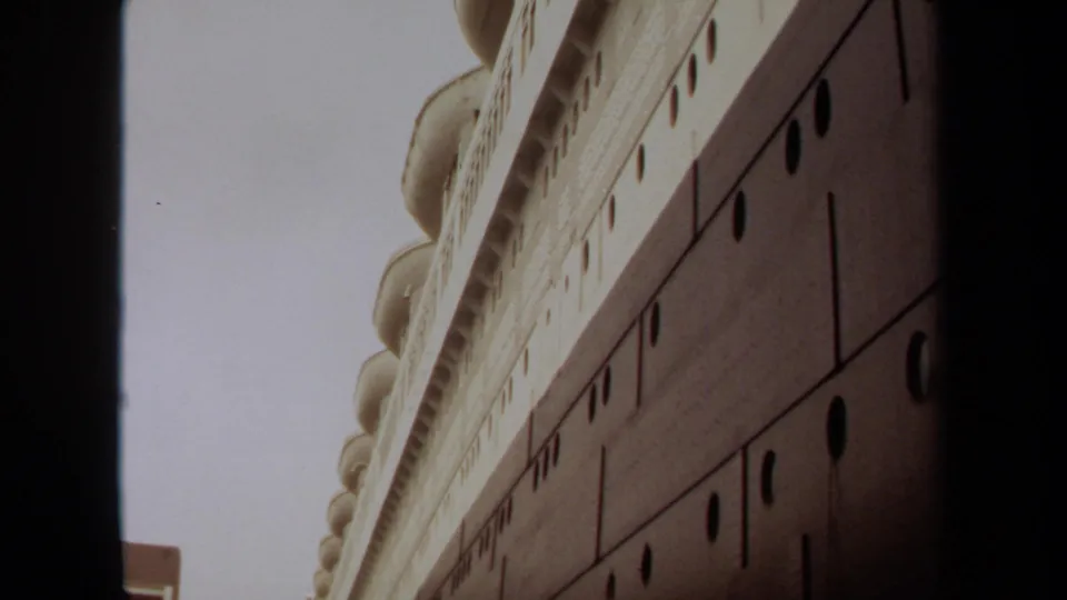 1971 Long Beach home-movie frame looking up along a large docked ship, emphasizing its dark hull, portholes, and white superstructure.
