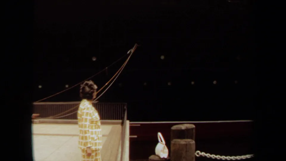 1971 Long Beach frame showing a woman on the pier looking up toward the large docked ship beside railing, posts, and mooring lines.