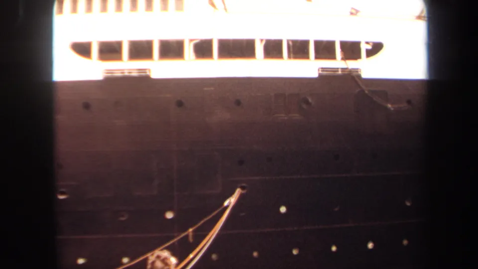 1971 Long Beach frame of the ship's side, showing dark hull plating, portholes, mooring lines, and a bright white upper deck section.
