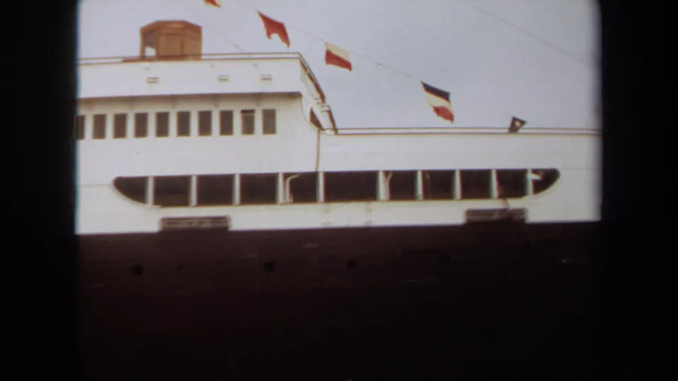 1971 Long Beach frame of the liner’s white upper decks, dark lower hull, deck windows, and multiple flags blowing along the top edge.