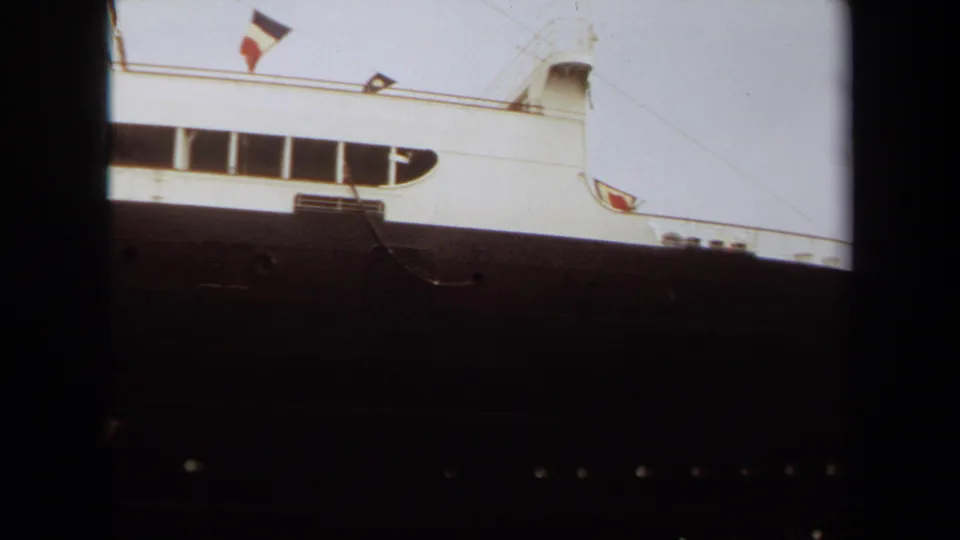 Final 1971 Long Beach frame with the liner cropped at the side, showing a flag above the white deck, long windows, and the dark hull beneath.