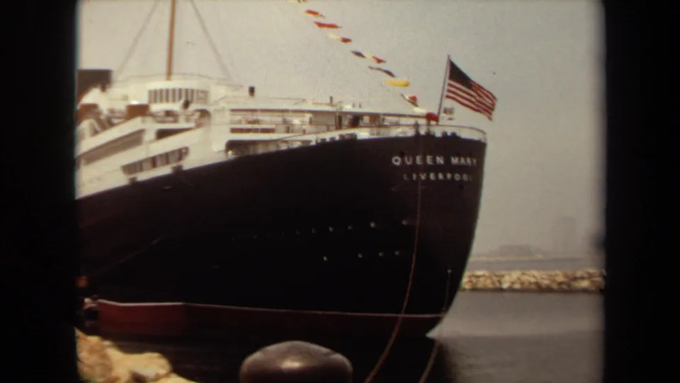 1971 Long Beach frame with QUEEN MARY LIVERPOOL lettering on the bow, an American flag, signal flags, and harbor rocks.