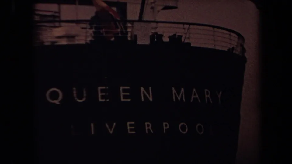 Dark 1971 Long Beach frame showing faint Queen Mary and Liverpool lettering, the bow silhouette, railings, and upper deck shapes.