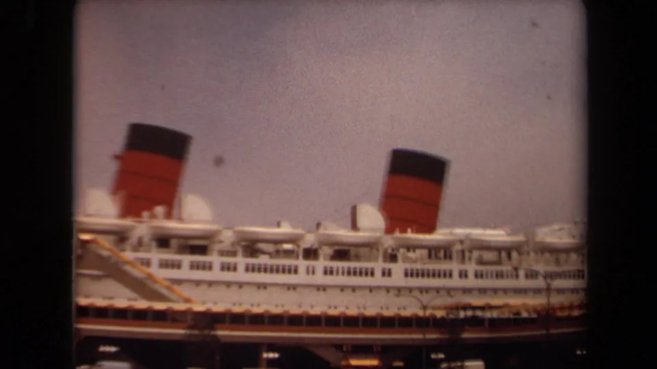 1971 Long Beach 8mm frame with the ship's white decks, red-and-black funnels, dock edge, and foreground streetlights.