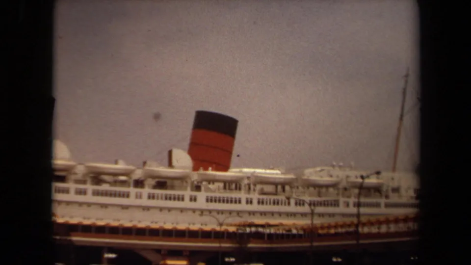 1971 Long Beach frame showing the liner's side, a prominent funnel, dock structures, streetlights, and a vertical pole near the edge.