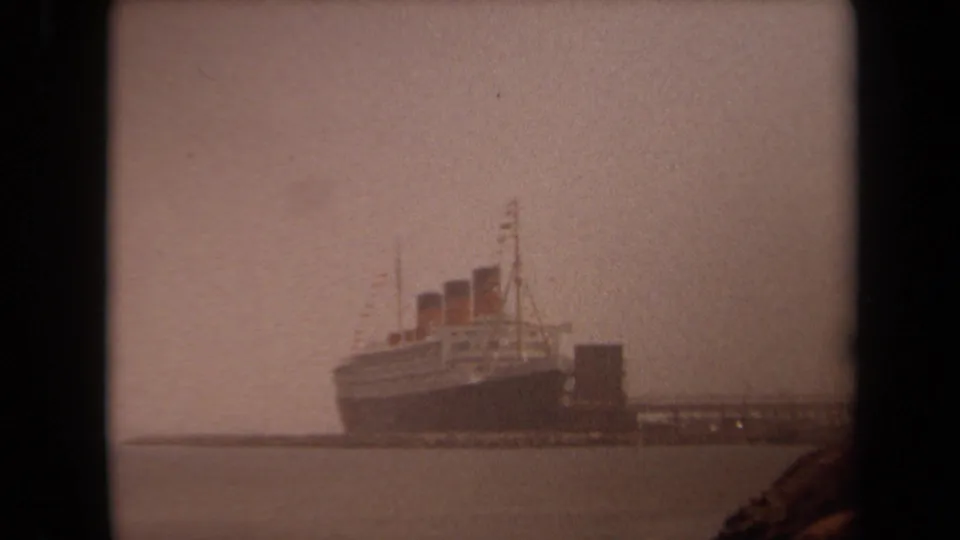 Distant 1971 Long Beach harbor view of a large liner with three funnels, seen through haze across calm water on 8mm film.