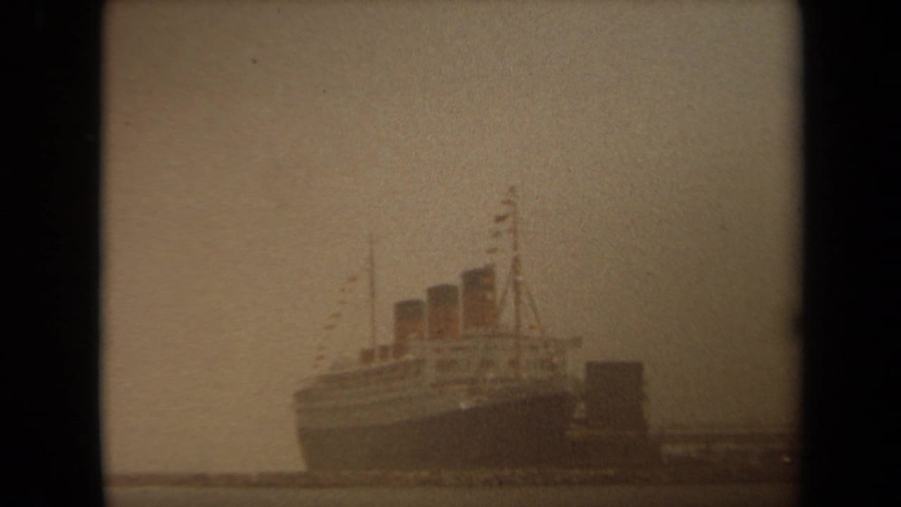 1971 Long Beach 8mm frame showing a large passenger ship with three smokestacks at a dock in hazy light.