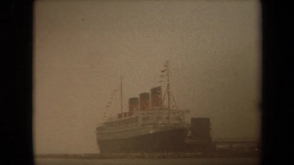 1971 Long Beach 8mm frame showing a large passenger ship with three smokestacks at a dock in hazy light.