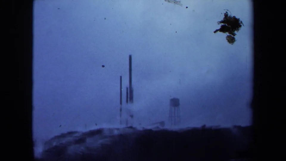 1971 Maine 8mm frame showing the same foggy industrial site with water tower and stacks, plus a prominent dark dirt mark near the top.