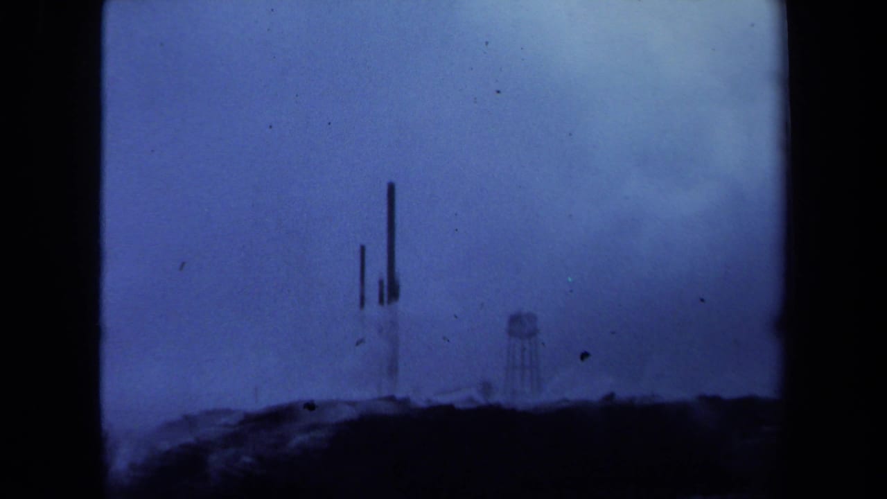 Distant metal towers and a water tower beyond a dark ridge under a cloudy blue sky.
