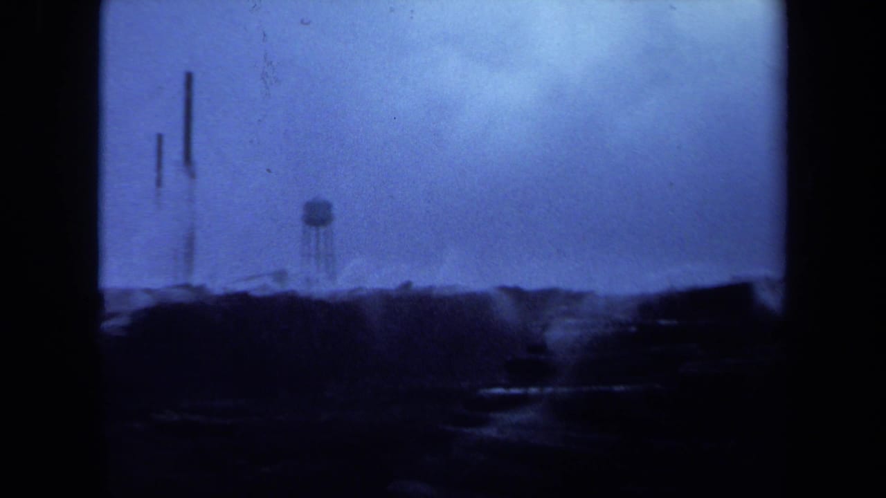 Blue-tinted dark shoreline with a distant water tower and film gate borders.
