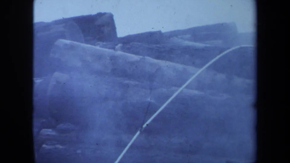 1971 Maine 8mm view of large cut logs filling the frame, softened by smoke, grain, and blue-tinted exposure.