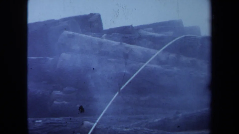 1971 Maine logging-site frame showing stacked cut logs and smoke, with worn film texture and no readable signage.