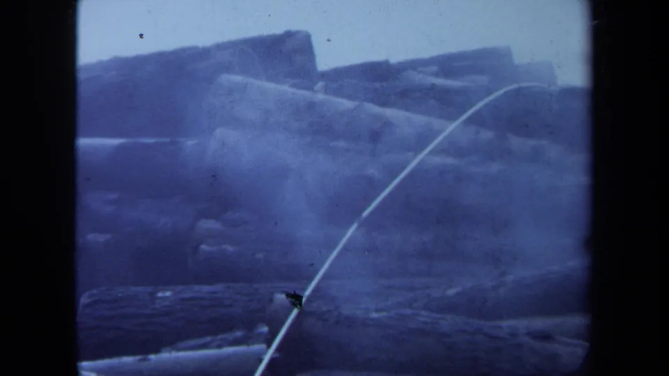 1971 Maine 8mm frame showing a large stack of logs with a pale rope or cable crossing diagonally through the scene.