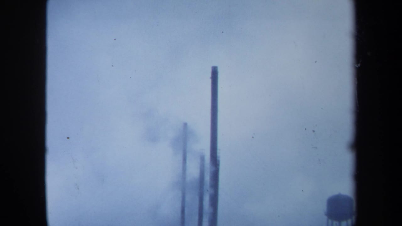 1971 Maine 8mm frame showing distant industrial stacks and smoky haze against a pale sky.