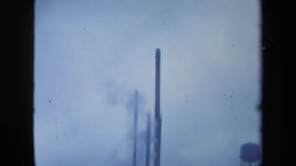 1971 Maine 8mm frame showing distant industrial stacks and smoky haze against a pale sky.