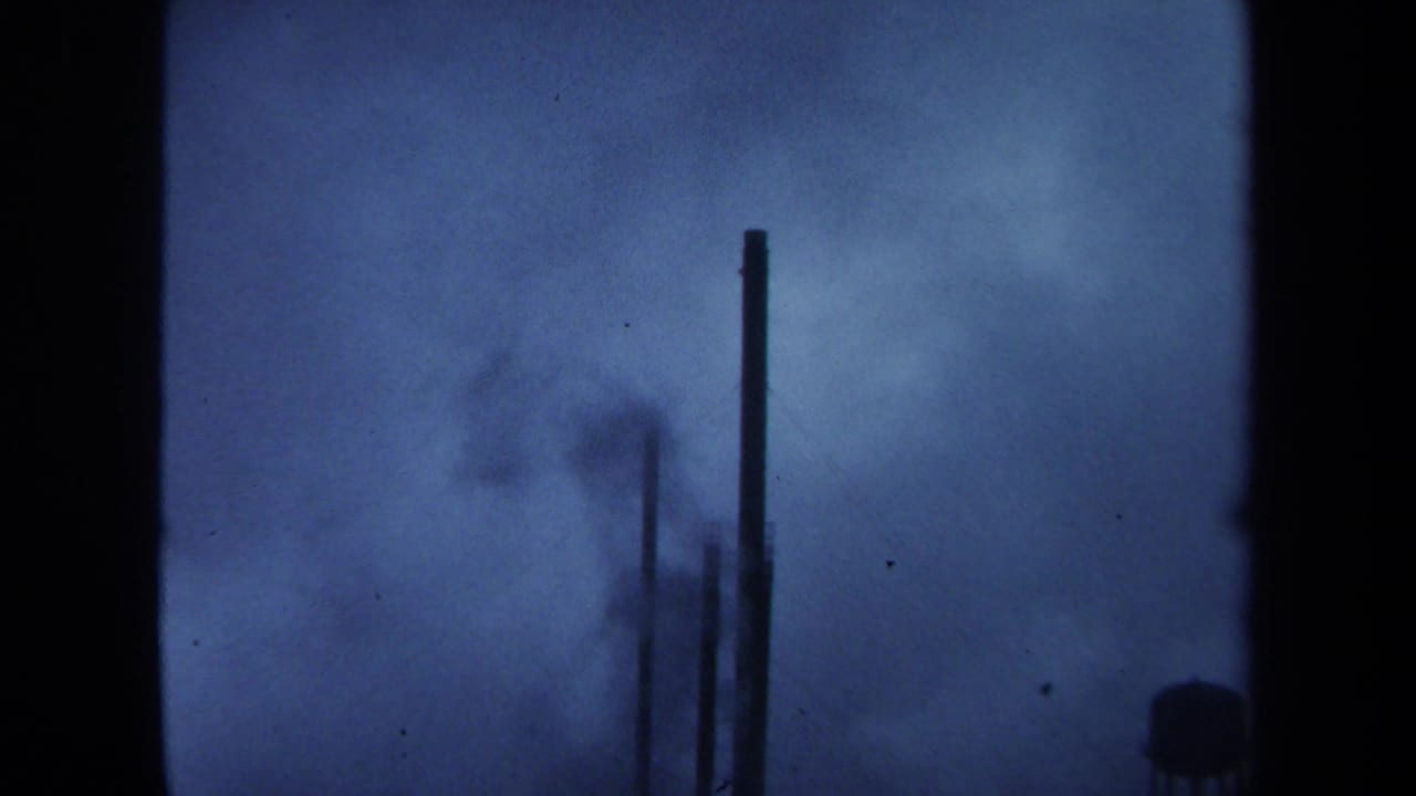 Tall smokestack silhouettes and smoke haze against a blue-toned sky.