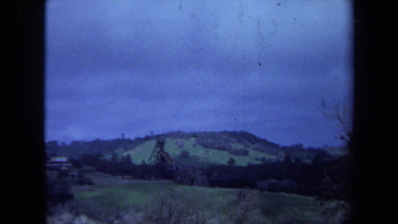 Rolling fields and wooded hills with a brown tower structure framed by dark film edges.