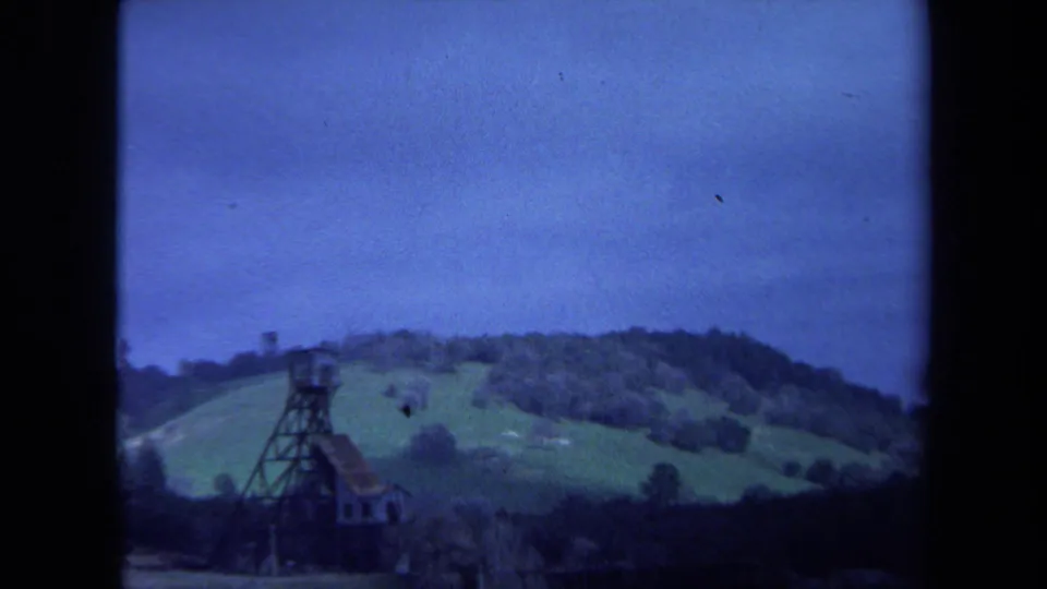 1971 Maine 8mm frame showing a tower beside open countryside, with wooded slopes and a blue overcast sky in the distance.