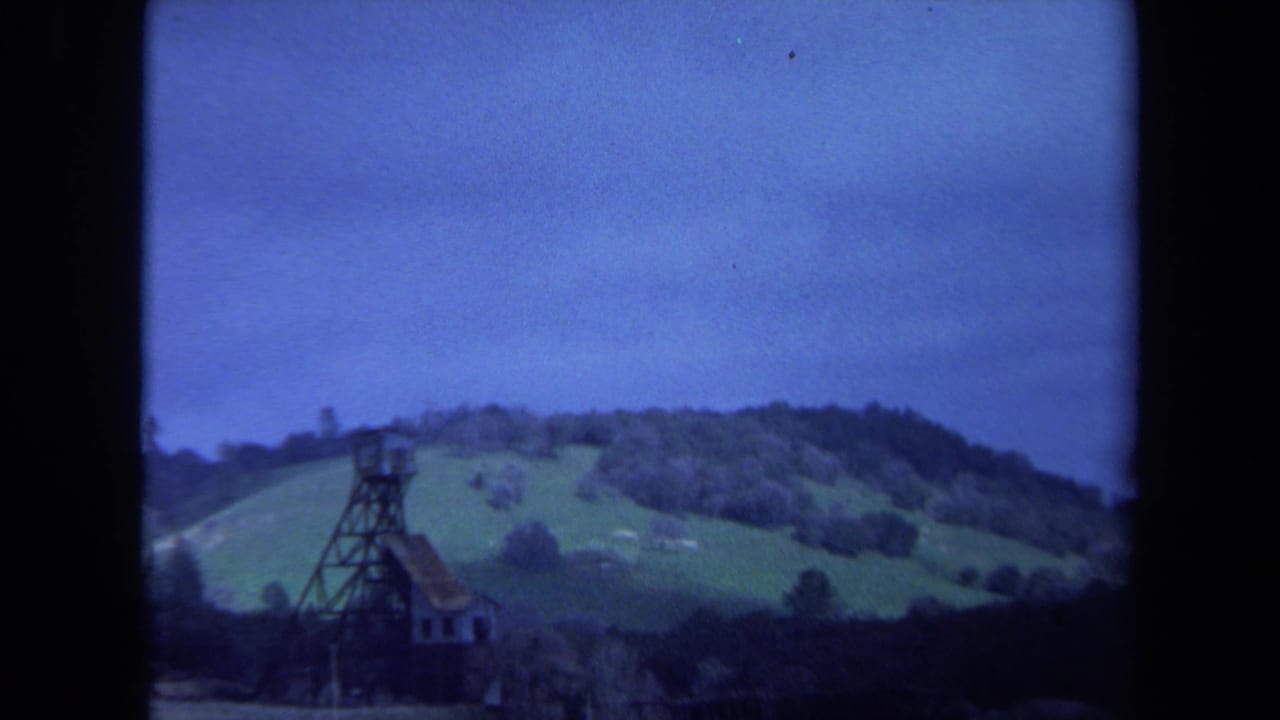 1971 Maine 8mm frame showing green hills, trees, and a dark tower structure beneath a cool blue sky.