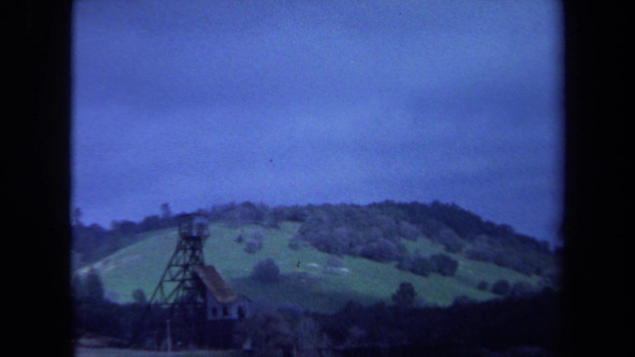 Distant tower on green hills with trees and cloudy sky.