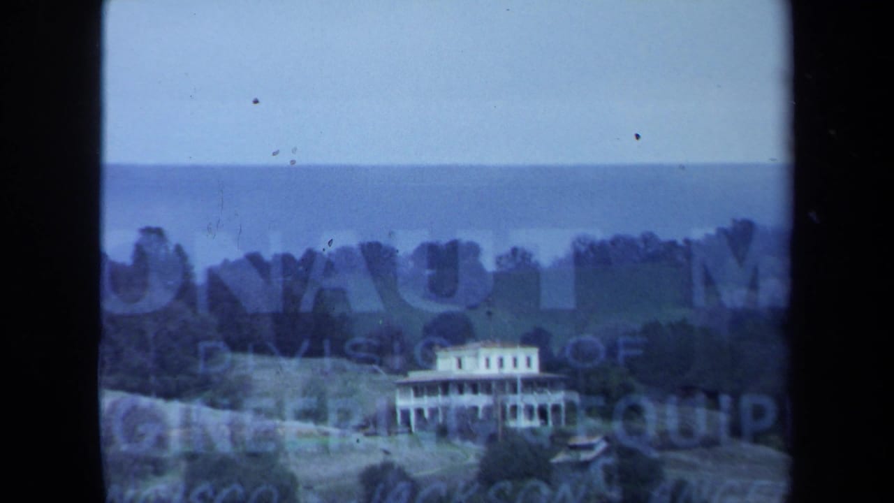Rural hillside with a large white house behind partially obscured sign lettering and film borders.