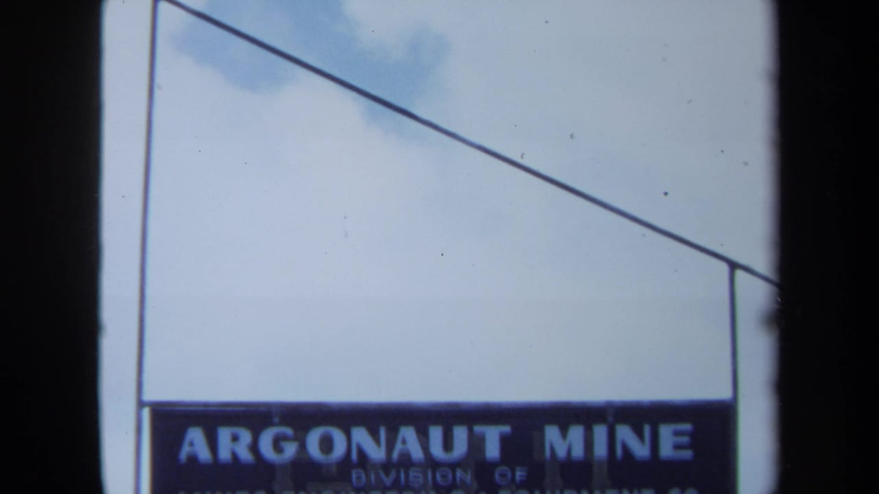 1971 Maine 8mm frame showing a weathered Argonaut Mine sign against pale blue sky and clouds.