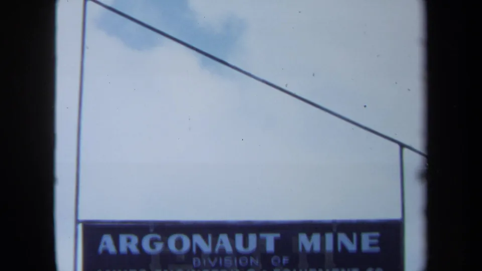 1971 Maine 8mm frame showing a weathered Argonaut Mine sign against pale blue sky and clouds.