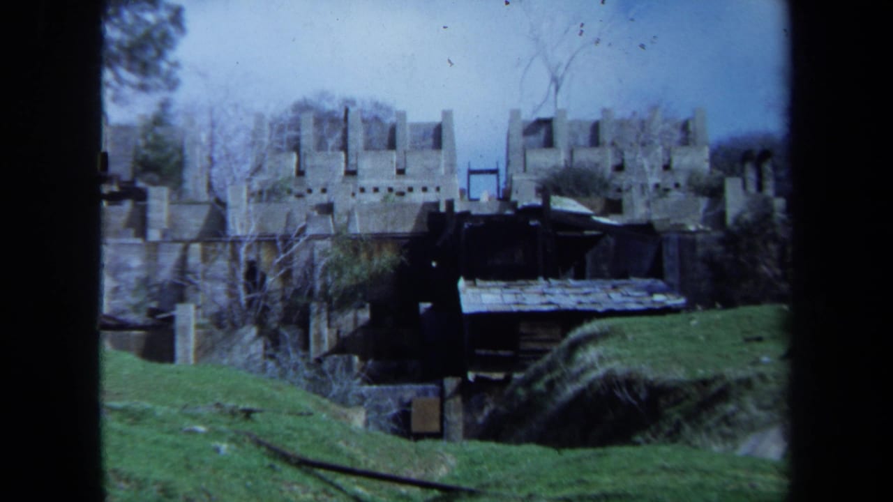 1971 Maine 8mm frame showing castle-like stone remains, bare trees, green grass, and a small dark shed in the foreground.