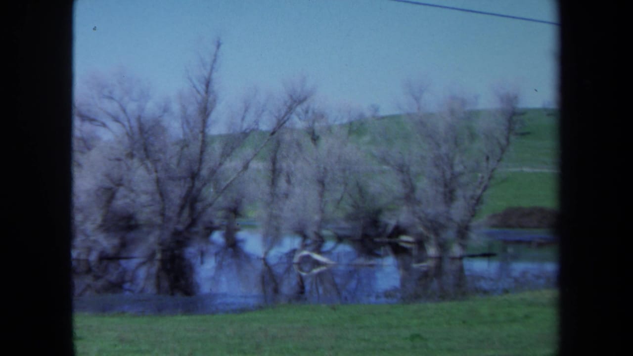 1971 Maine 8mm frame showing still floodwater around bare trees, with a grassy hill and diagonal power line beyond.