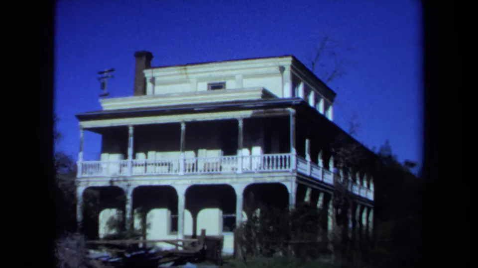 1971 Maine 8mm frame centered on a large light-colored house with arched lower porch openings, white railings, chimney, and trees around it.